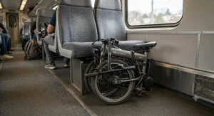 A folded electric bike neatly stowed under a commuter train seat, showing its space-saving design.
