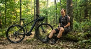 A happy cyclist smiling while taking a break on a woodland path with their hardtail emtb under $2000.