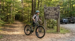 A beginner cyclist parking their hardtail eMTB next to a national forest trailhead sign in the United States.