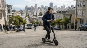 An adult riding a dual motor electric scooter up a steep San Francisco street during the afternoon commute.