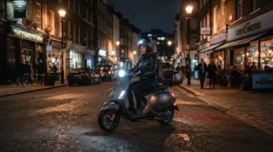 Riding a dual motor electric scooter equipped with bright headlights along a lit city street at night.
